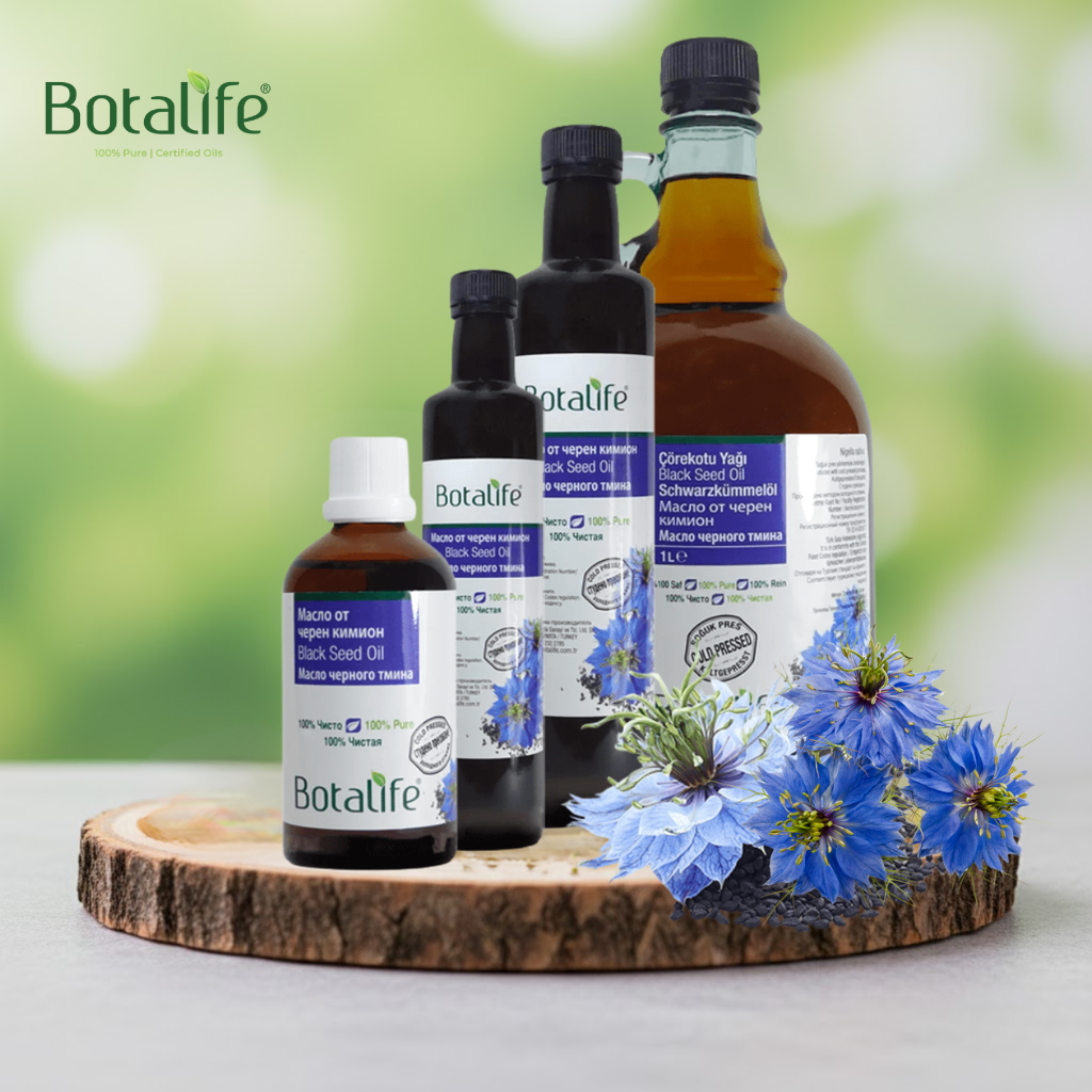 Лечебните свойства на маслото от черен кимион – бутилки масло от черен кимьон и цветове Nigella sativa на дървена подложка, Botalife